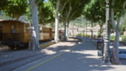 Blurred view of an outdoor train station in mallorca with a wooden train in the background and sunlight filtering through the trees