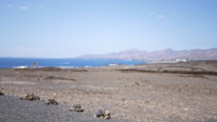 Blurred and out of focus image of an arid countryside field with distant mountains and a bokeh effect under clear blue skies