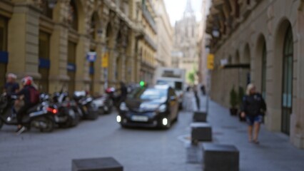 Blurry street scene in barcelona with people, vehicles, and historic architecture captured in soft focus, creating a vibrant urban atmosphere.