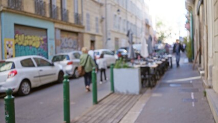 Blurred street scene in marseilles with people walking by graffiti-covered walls and parked cars,...