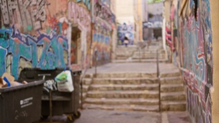 Blurred alleyway showcases vibrant street graffiti and garbage bins in an urban ghetto setting, emphasizing the gritty, defocused atmosphere of an outdoor city street. © Krakenimages.com