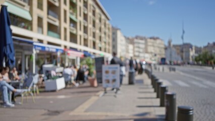 Blurred scene featuring people walking and sitting outdoors on a sunny street in marseilles, france, with defocused buildings and vibrant bokeh effects capturing urban life.