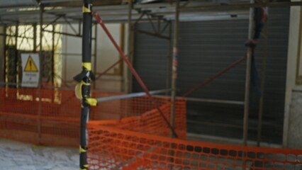 Blurred construction site with orange safety netting and scaffolding highlighting bokeh effect and defocused warning sign in background.