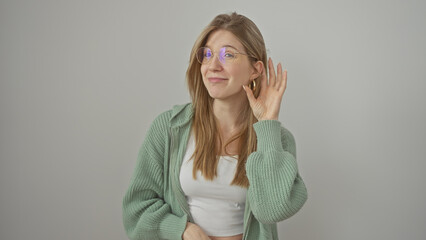 A young woman with blonde hair, wearing glasses and a green sweater, listening over a white...