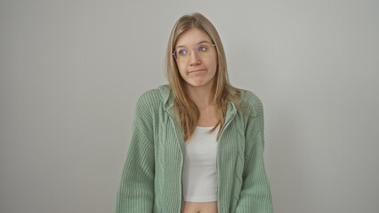 Obraz premium Young blonde woman in glasses and green sweater posing with a neutral expression against a white isolated background