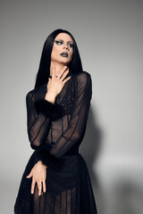 Fototapeta premium A fashionable drag queen showcases a stunning black outfit against a soft grey backdrop, exuding confidence.