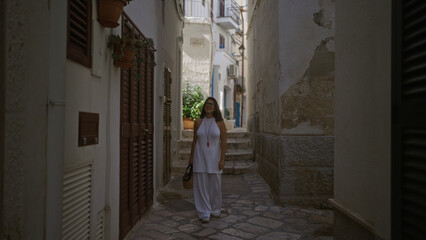 A young hispanic woman walks along the beautiful narrow streets of polignano a mare, puglia, italy, enjoying a sunny day in europe.