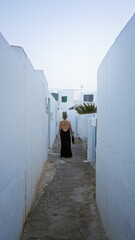 Woman walking through narrow alleyway in famara, lanzarote, with white buildings surrounding and clear sky above