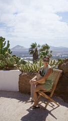 Woman relaxing outdoors in lagomar, lanzarote, canary islands, with cacti, mountains, and palm trees in the background, enjoying a sunny day