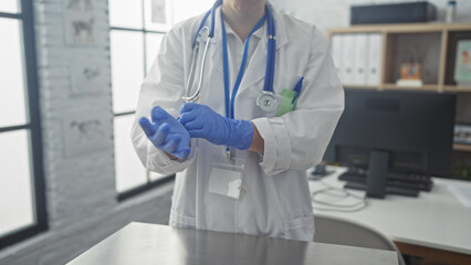 A female doctor in a clinic room preparing for an examination by putting on blue gloves, with a stethoscope around her neck.