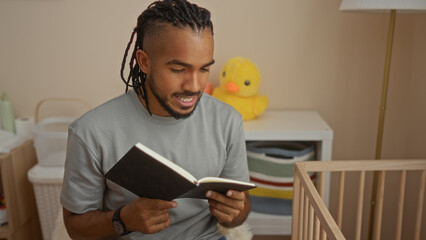 Young man with braids reading in a cozy bedroom beside a baby cradle, creating a serene and intimate home setting indoors with thoughtful expression.