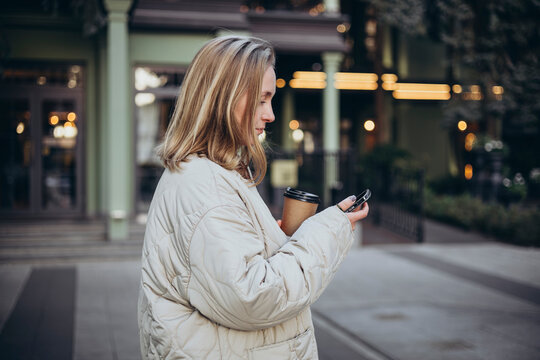 A young woman uses a smartphone and drinks coffee on the way to work.