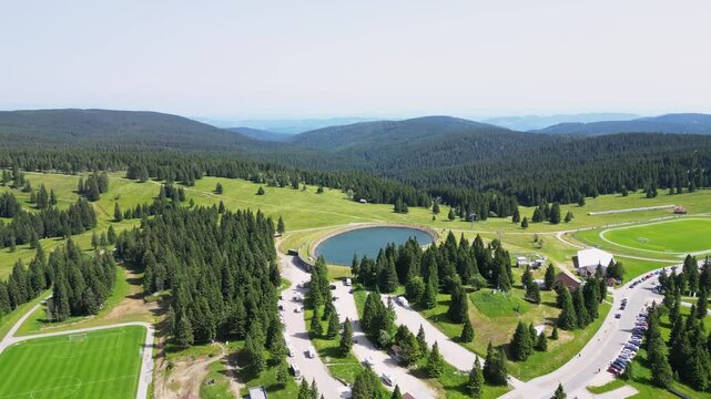 Aerial view of serene mountain landscape with a tranquil lake, forest, and road, Rogla, Slovenia.