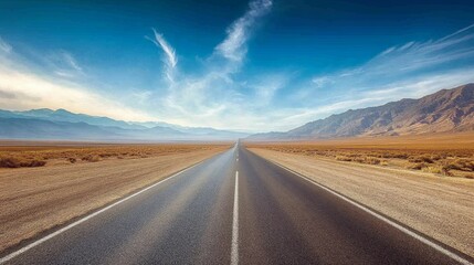 Naklejka premium A serene, empty road stretches into the horizon under a clear blue sky, surrounded by mountains and vast, open land.