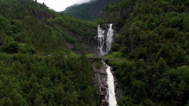 Aerial view of skjervfossen waterfall cascading through lush green forest and majestic mountains, Granvin, Norway.