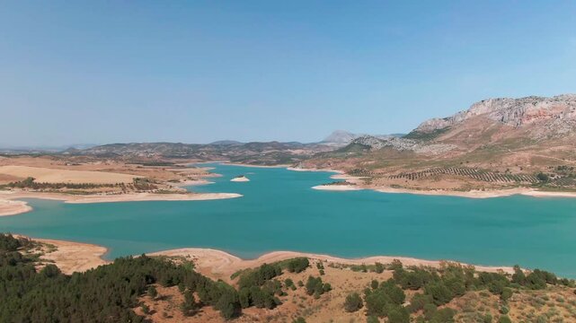 Aerial view of serene Tres Embalses lake surrounded by picturesque mountains and blue sky, Campillos, Spain.