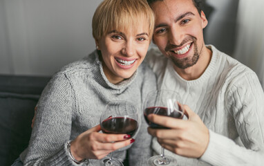 Cheerful couple enjoying a glass of red wine together, smiling and celebrating indoors. Warm, cozy atmosphere with love and happiness.