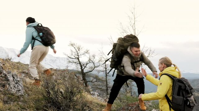 Side view at group of four hikers with backpack overcoming trekking trail along rocks at scenic mountain landscape. Tourist path with teamwork, support and unity