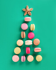 Obraz premium Multicolored macarons in the form of a Christmas tree with star on a green background. Vertical orientation, top view.