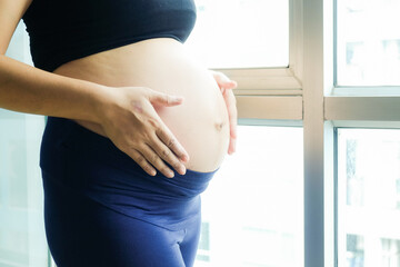 Pregnant asian women standing with window light shw belly