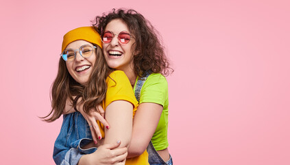 Two happy friends hugging and laughing together, wearing colorful clothing and trendy glasses,...