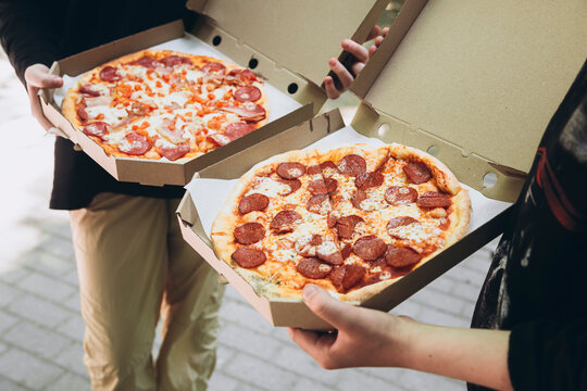 Teenagers with pizza in cardboard boxes on a walk in the park. Appetizing salami pizza close-up. Teenagers eat fast food. Food delivery, takeaway pizza.