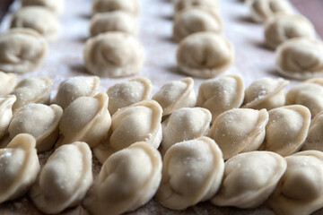 The raw dumplings were placed on a wooden cooking board, sprinkled with flour. The filling is minced meat, potatoes, cheese or cottage cheese. A semi-finished product, ready for cooking.