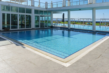 A serene swimming pool beside a modern building, reflecting clear blue skies in summer sunlight.