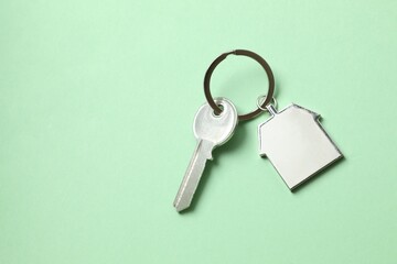 Metallic key with keychain in shape of house on color background