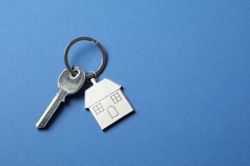 Metallic key with keychain in shape of house on color background