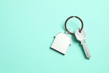 Metallic key with keychain in shape of house on color background