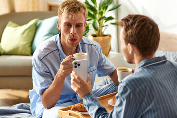Obraz premium A loving gay couple relaxes together in their pajamas, sipping coffee