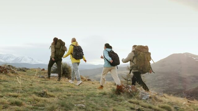 Group of four hikers with backpack together go trail forward high up at scenic mountain landscape views. Active uphill path, climbing way and travel recreation