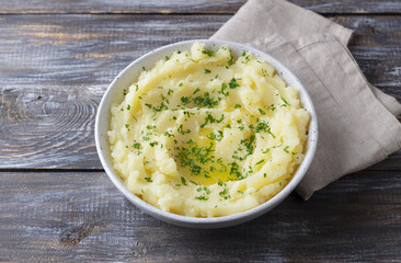 Mashed potatoes with melted butter and herbs in a gray ceramic bowl on a wooden table