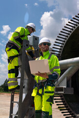 Maintenance engineer team standing at windmills at wind turbine farm. Skill people working outdoors at alternative renewable energy wind power station. Sustainable clean energy technology. Ecology