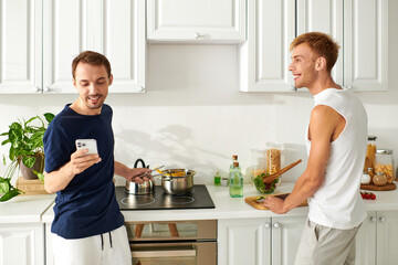 Two men cheerfully cooking together in a modern kitchen, embracing their love and creativity.