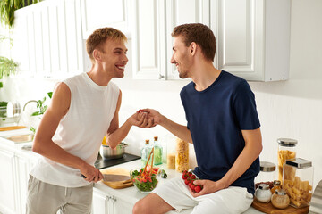 Two men joyfully chop vegetables for a salad, sharing smiles in their stylish and inviting kitchen.