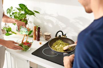 Two men joyfully prepare a colorful lunch while cooking pasta in their vibrant, modern kitchen.