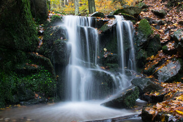 A forest stream with a waterfall in autumn, surrounded by vibrant colorful leaves.