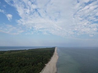 Aerial View of Coastline with Dense Forest, Calm Sea, and Clouds in the Sky