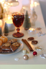 Various Christmas decorations, cookies, chocolate, nuts and tangerines, wine glasses and lit candles on the table. Holiday hygge at home. Selective focus.