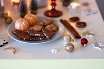 Various Christmas decorations, cookies, chocolate, nuts and tangerines, wine glasses and lit candles on the table. Holiday hygge at home. Selective focus.