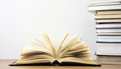 open book on wooden desk with stack of books beside it, showcasing knowledge and learning. pages are fanned out, inviting readers to explore