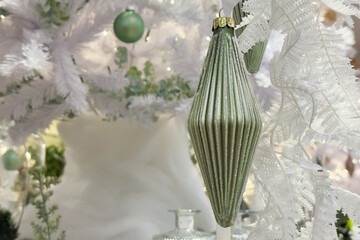 Close-Up Of A Green Ribbed Christmas Ornament Hanging On A White Christmas Tree, Creating A Festive Atmosphere