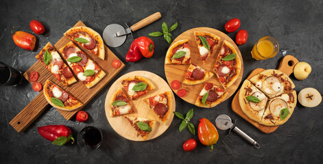 Pizza with pepperoni basil and tomatoes on boards on a dark background