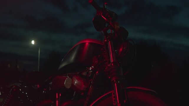 Close-up of motorcycle parked at night in patch of reflected of red light. Slow motion. Motorcycles have become not only means of transportation, but also eal symbol of freedom, speed and adventure