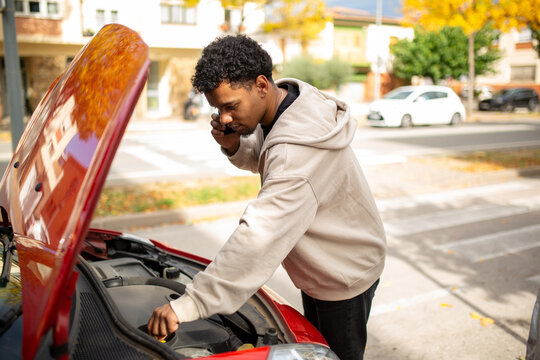 Man inspecting car engine while on phone