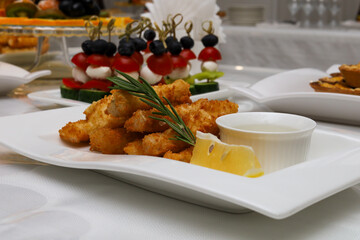 Fried fish slices with sauce, lemon and a sprig of rosemary on a white plate