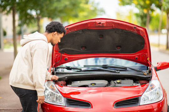 Man inspecting engine of red car with open hood on roadside