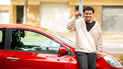Smiling man holding car keys next to red car on street